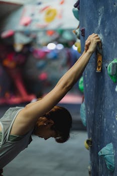 A female climber stretches on an indoor climbing wall, preparing for a workout.