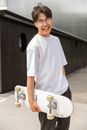 Joyful ethnic male teenager carrying skateboard and laughing after training in park