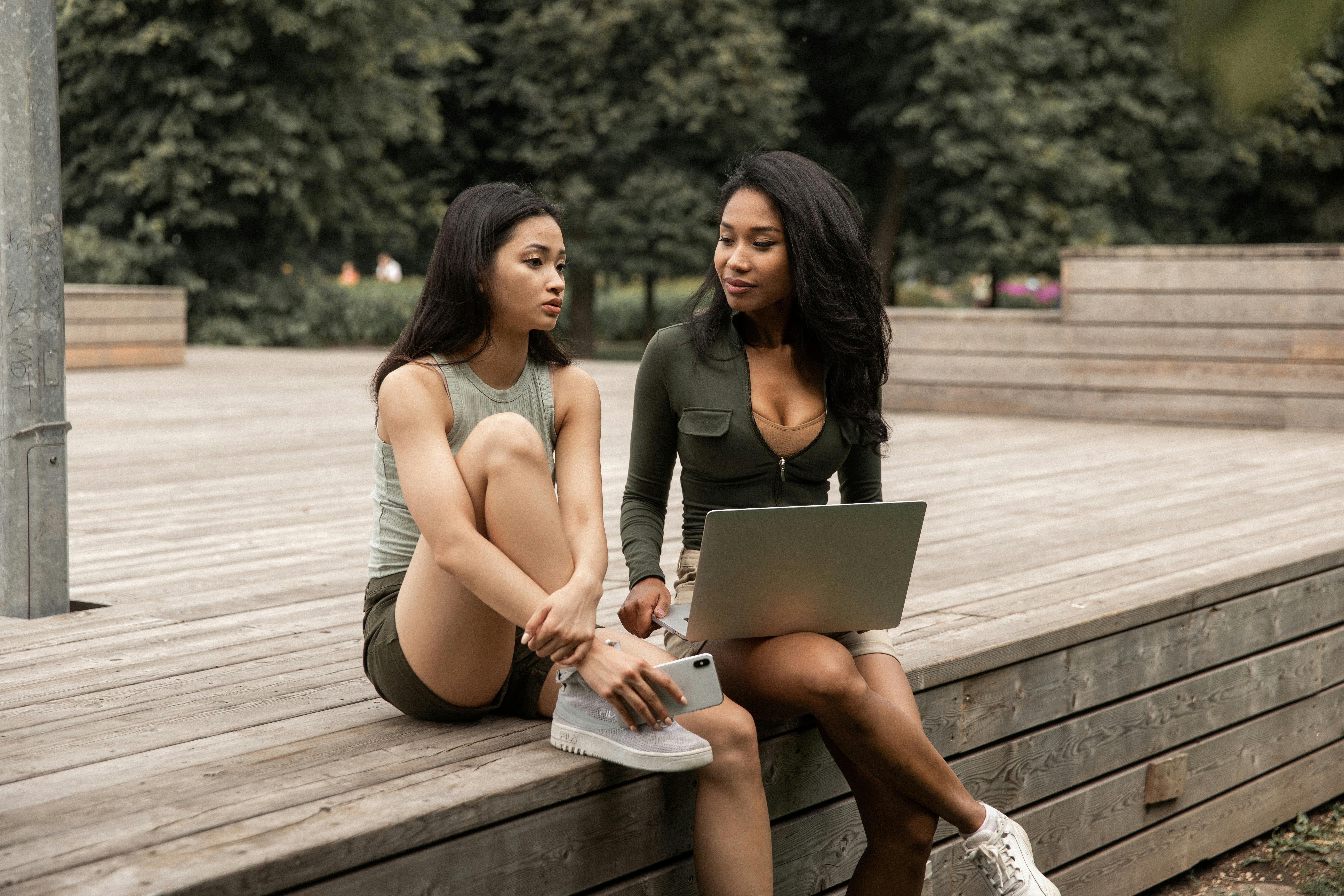 serious young multiracial ladies sharing laptop and chatting in park