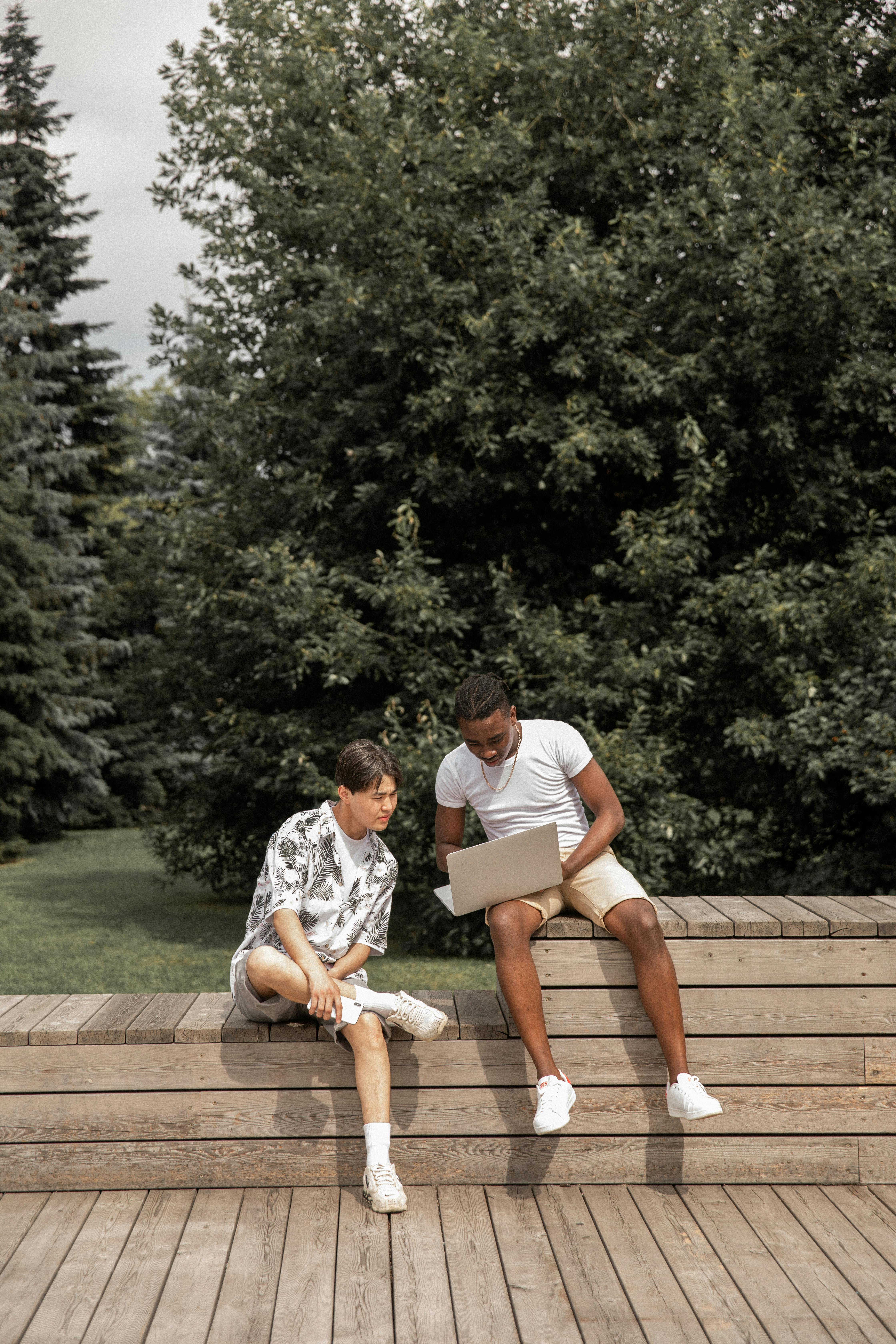 stylish young multiracial guys resting in park and sharing laptop