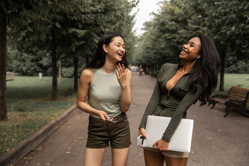 Two friends laughing together on a tree-lined path, photo by Monstera Production on Pexels