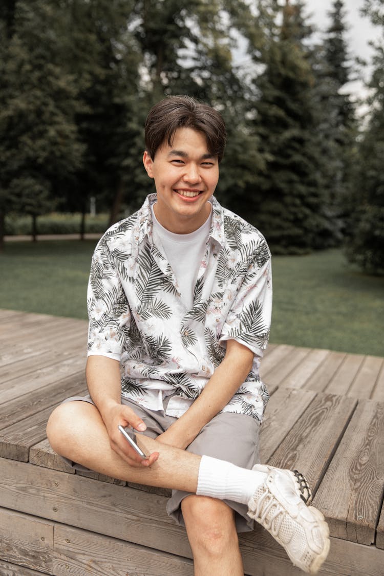 Happy Young Asian Male Smiling While Chilling On Bench In Park