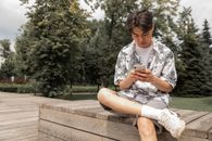 夏日里，年轻人坐在公园的长凳上，用智能手机享受着时光