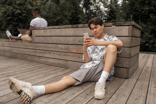 Casual young man concentrating on smartphone in a park setting, enjoying a summer day outdoors.