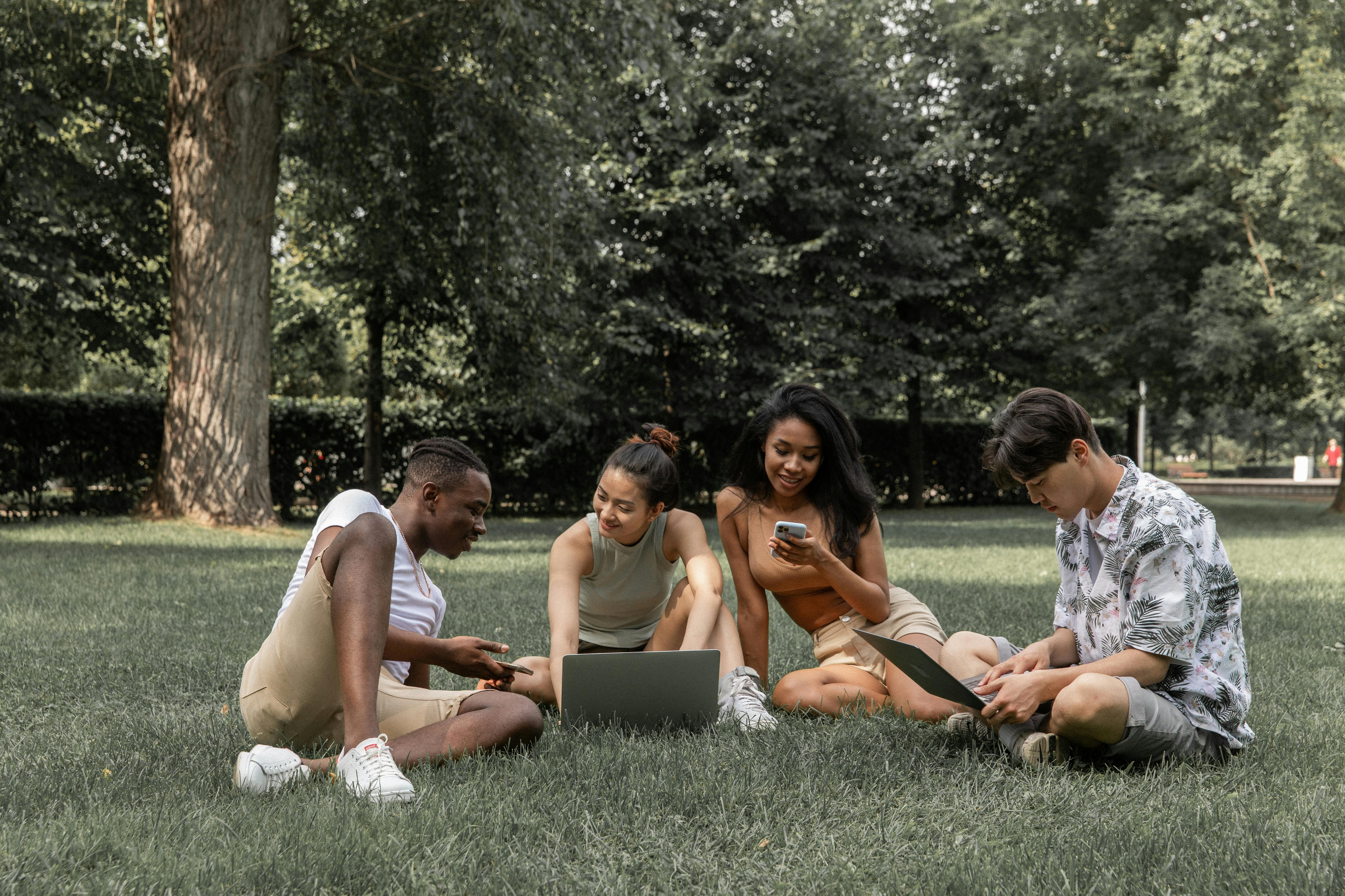 multiethnic friends with gadgets on lawn