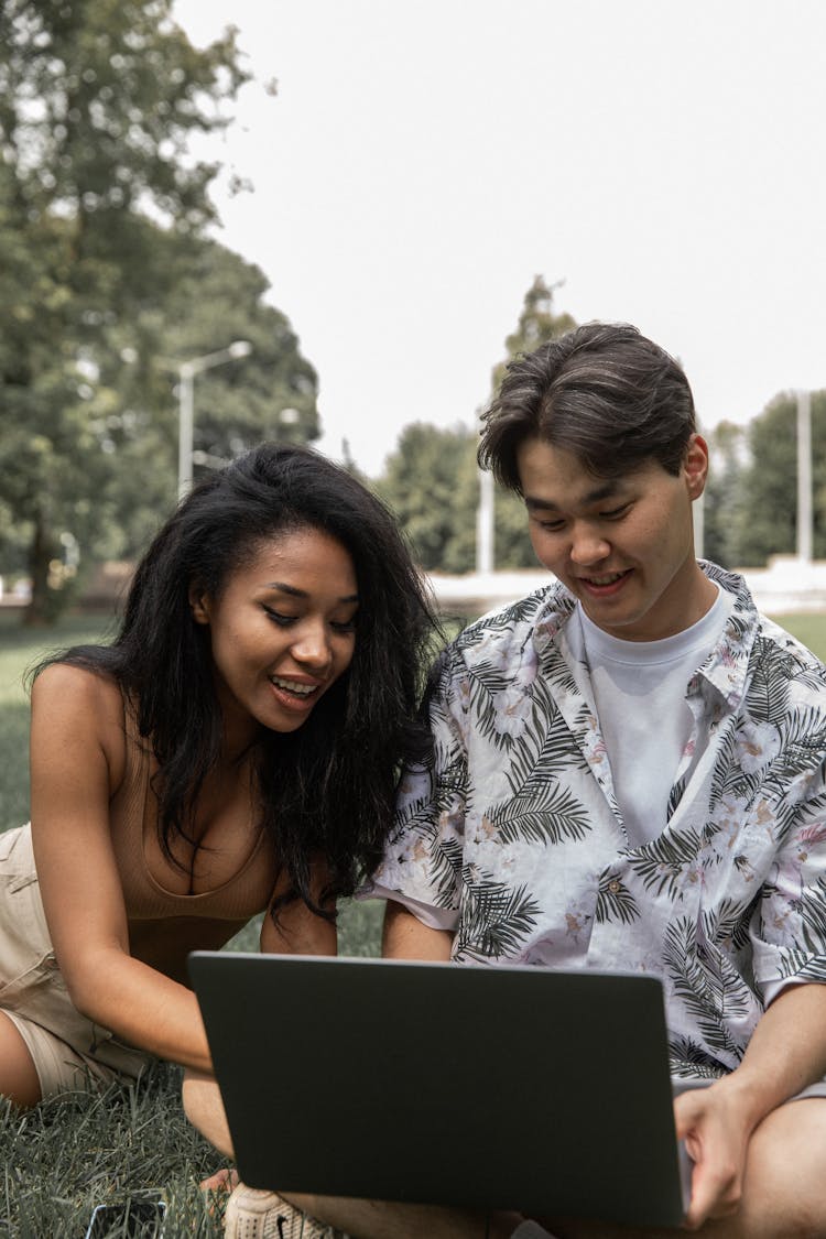 Cheerful Diverse Couple With Laptop On Lawn