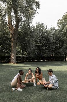 一群快乐的多种族朋友夏天穿着现代设备在草坪上度过时光