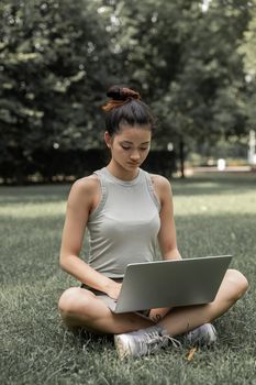 夏天，一位自信的年轻女子坐在公园的草地上使用笔记本电脑
