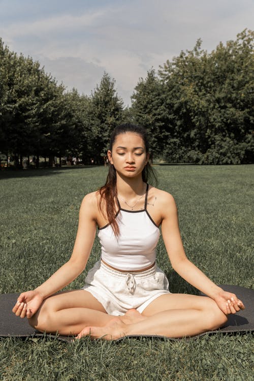 Free Full length of barefoot Asian female meditating in lotus pose with closed eyes on lawn Stock Photo