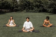 Full length of peaceful people in sportswear sitting in Padmasana with closed eyes and meditating in summer garden