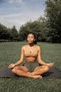 Full length of barefoot ethnic female in activewear sitting in lotus pose with closed eyes while listening to music in earbuds and meditating