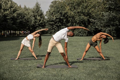 Group of diverse people in activewear stretching body while practicing Parivrtta Trikonasana in summer park