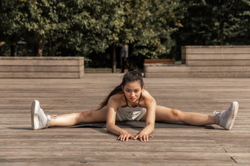 Full length of concentrated ethnic female in sportswear performing wide splits while practicing yoga in summer park