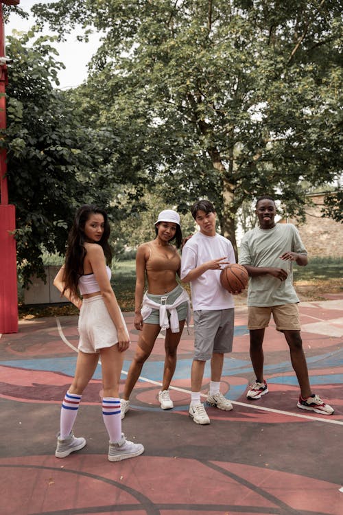 Group of multiracial friends in sportswear standing on basketball court with ball and looking at camera