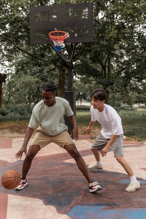 Full body focused young multiethnic sportsmen in activewear playing basketball together on sports ground on clear summer weather