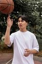 在郁郁葱葱的夏季公园里，一位穿着白衬衫的年轻健美亚洲男性正在旋转篮球进行训练