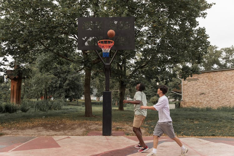 Diverse Sporty Men Throwing Basketball Ball Into Hoop On Court