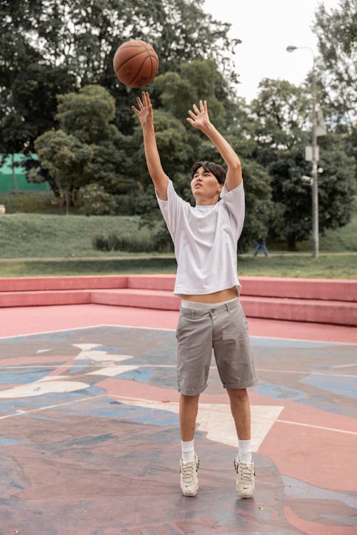 Asian man throwing basketball ball on sports ground