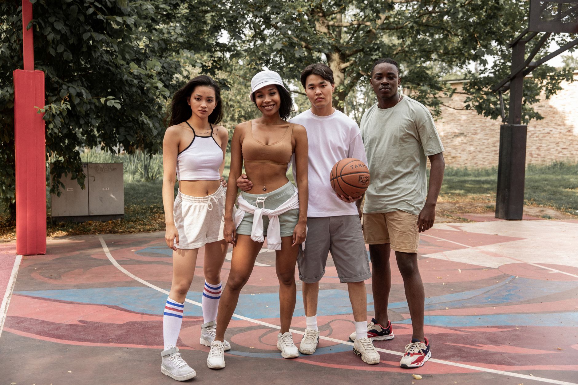 Young multiethnic friends in sportswear standing confidently on sports ground in city park with basketball ball and looking at camera contently