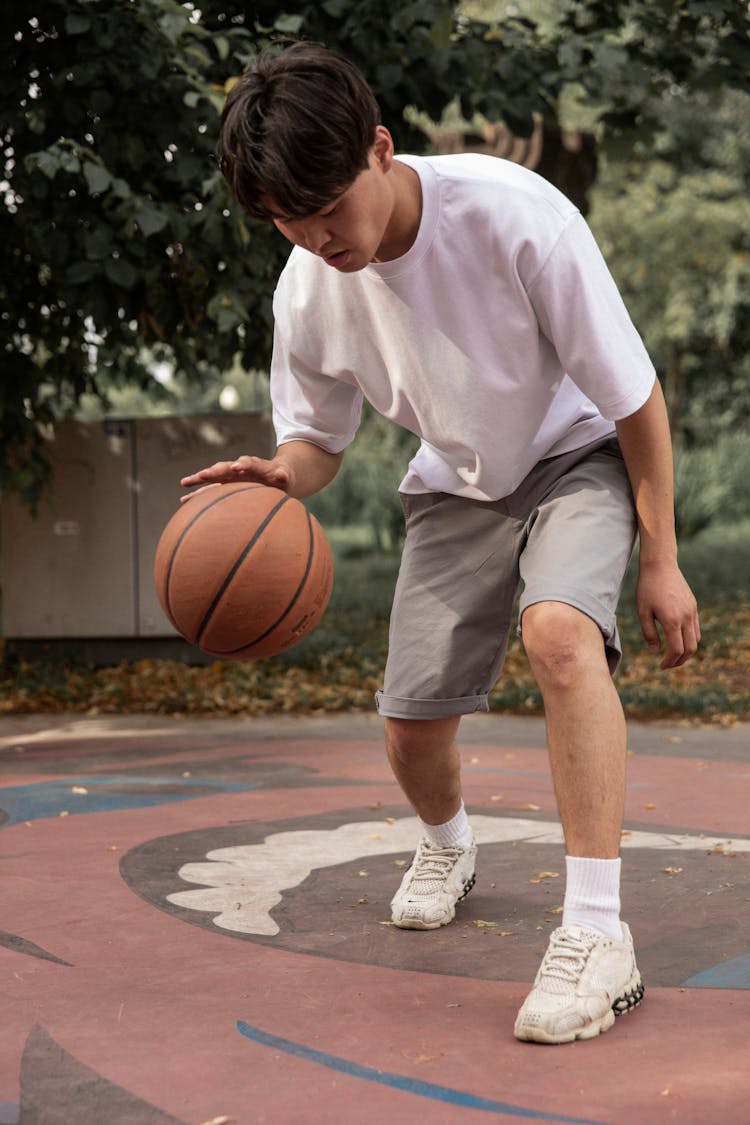 Focused Asian Man Dribbling Basketball Ball On Court