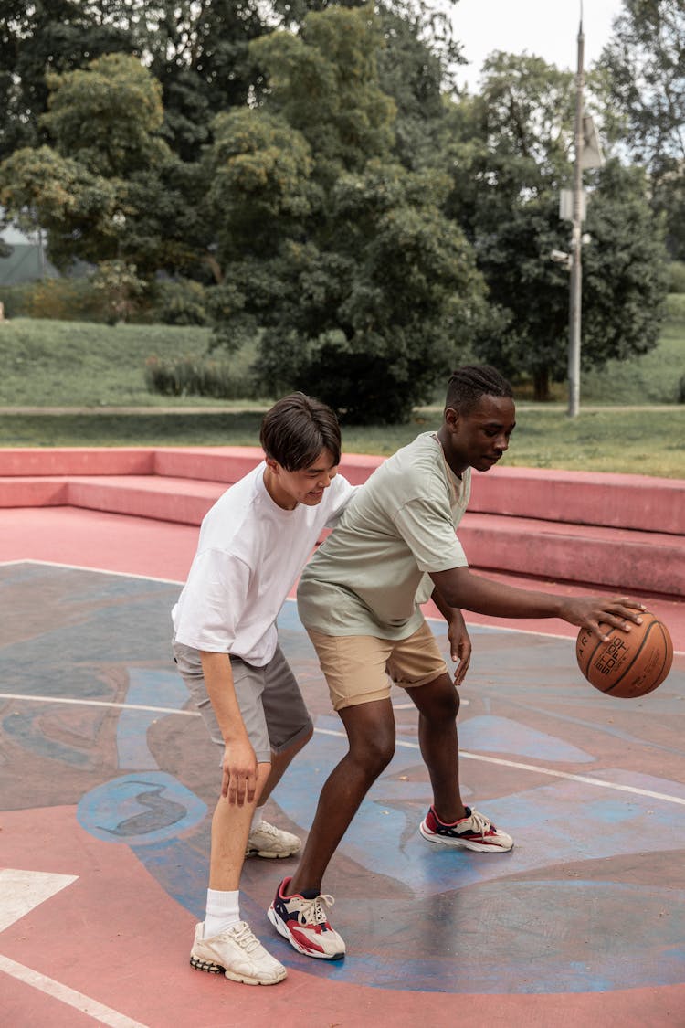 Young Diverse Sportsmen Playing Basketball On Court In Park