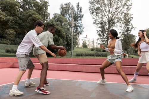Free Cheerful young multiracial sportspeople in activewear playing basketball on sports ground in lush city park Stock Photo