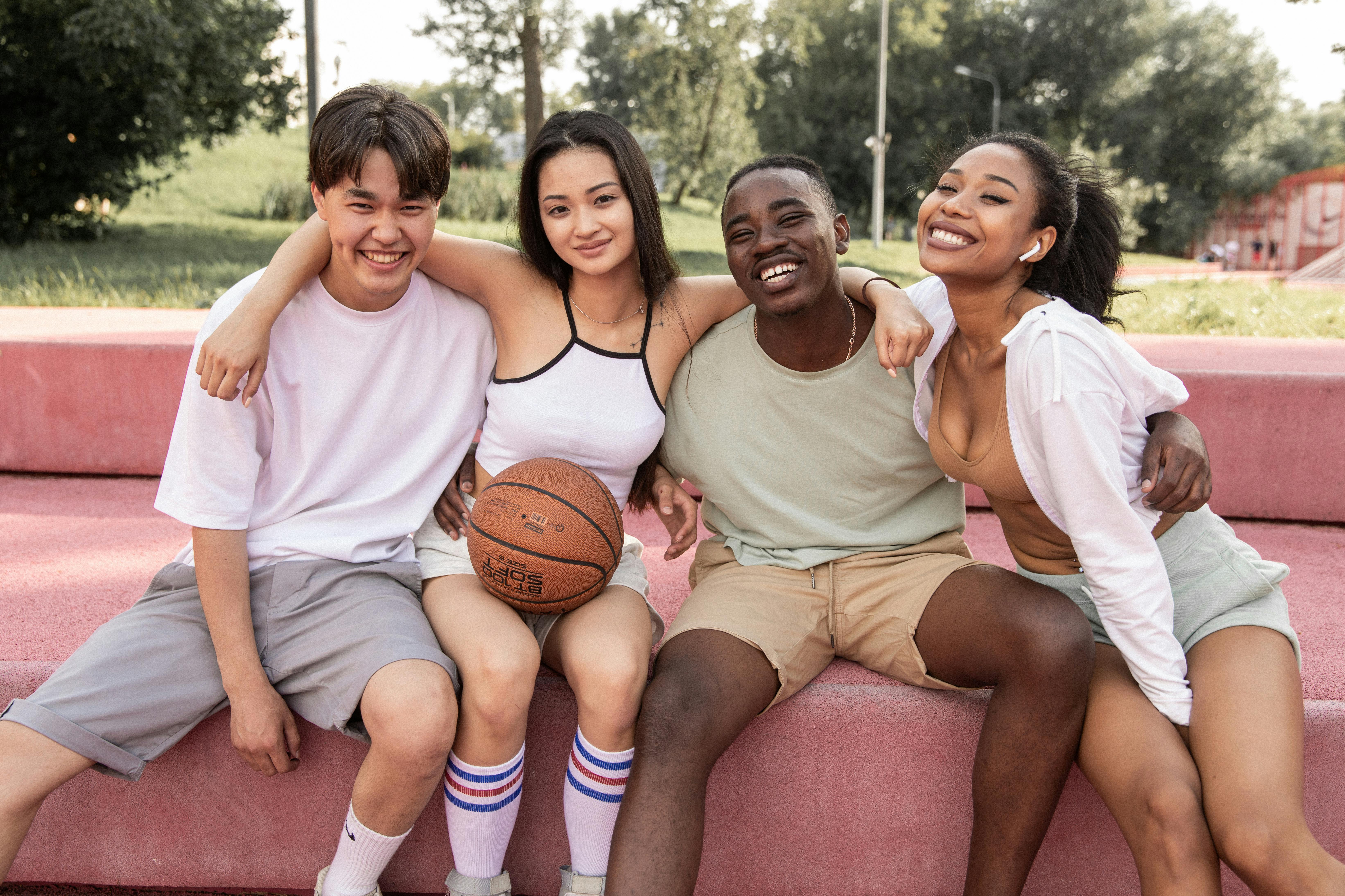 joyful multiethnic friends hugging on bench in park