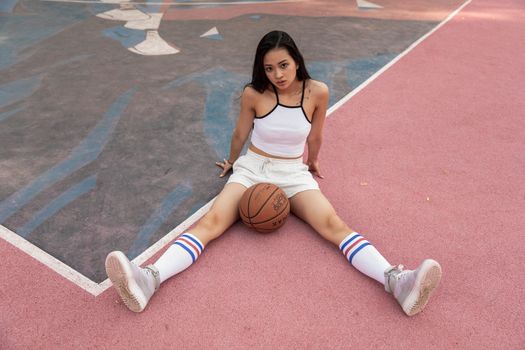 一名年轻女子穿着运动服，坐在户外篮球场上，显得自信又时尚