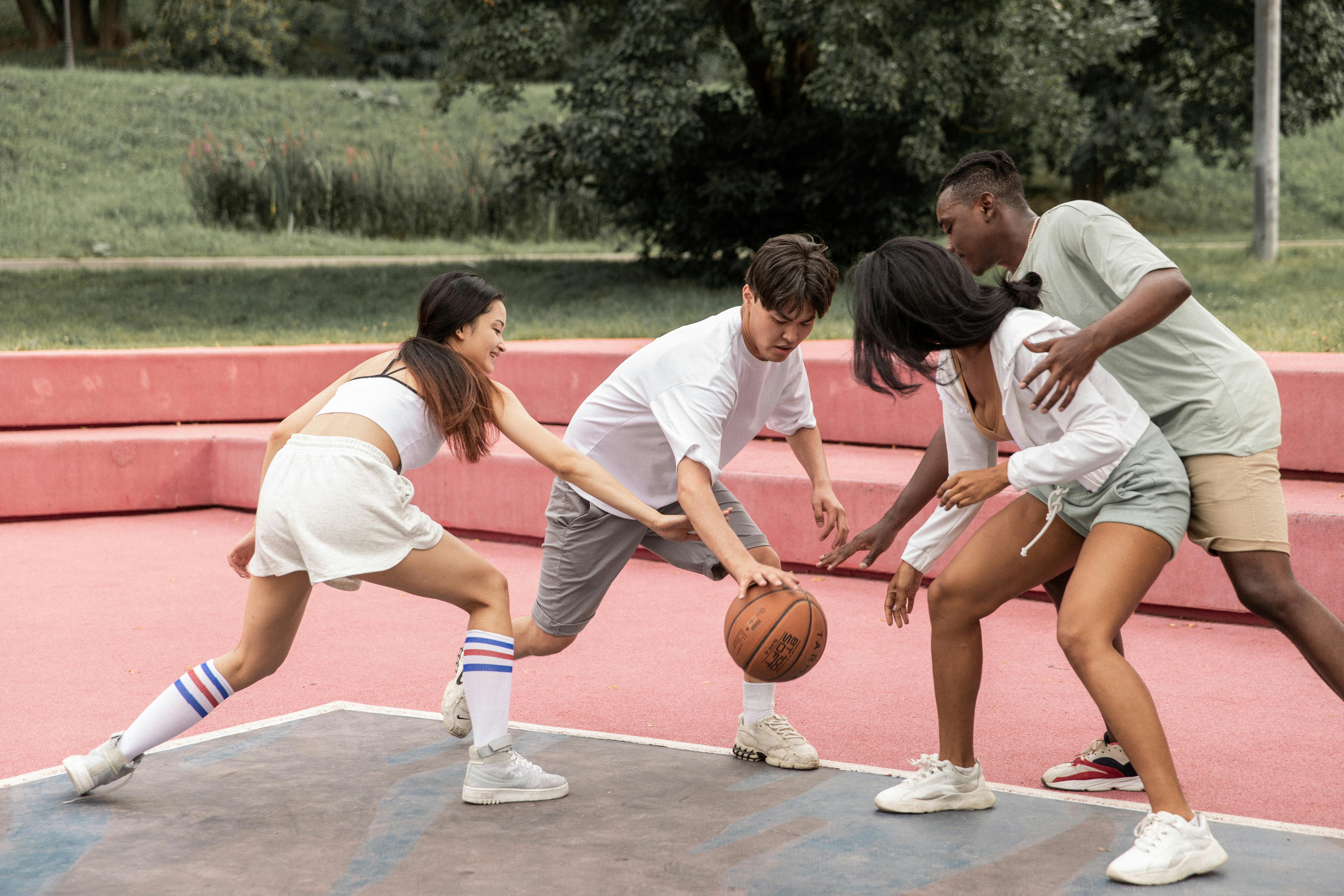 positive young diverse teenagers playing basketball on outdoor court