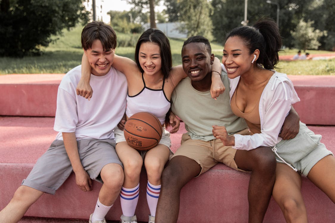 Free Happy multiracial friends embracing on bench after basketball training Stock Photo