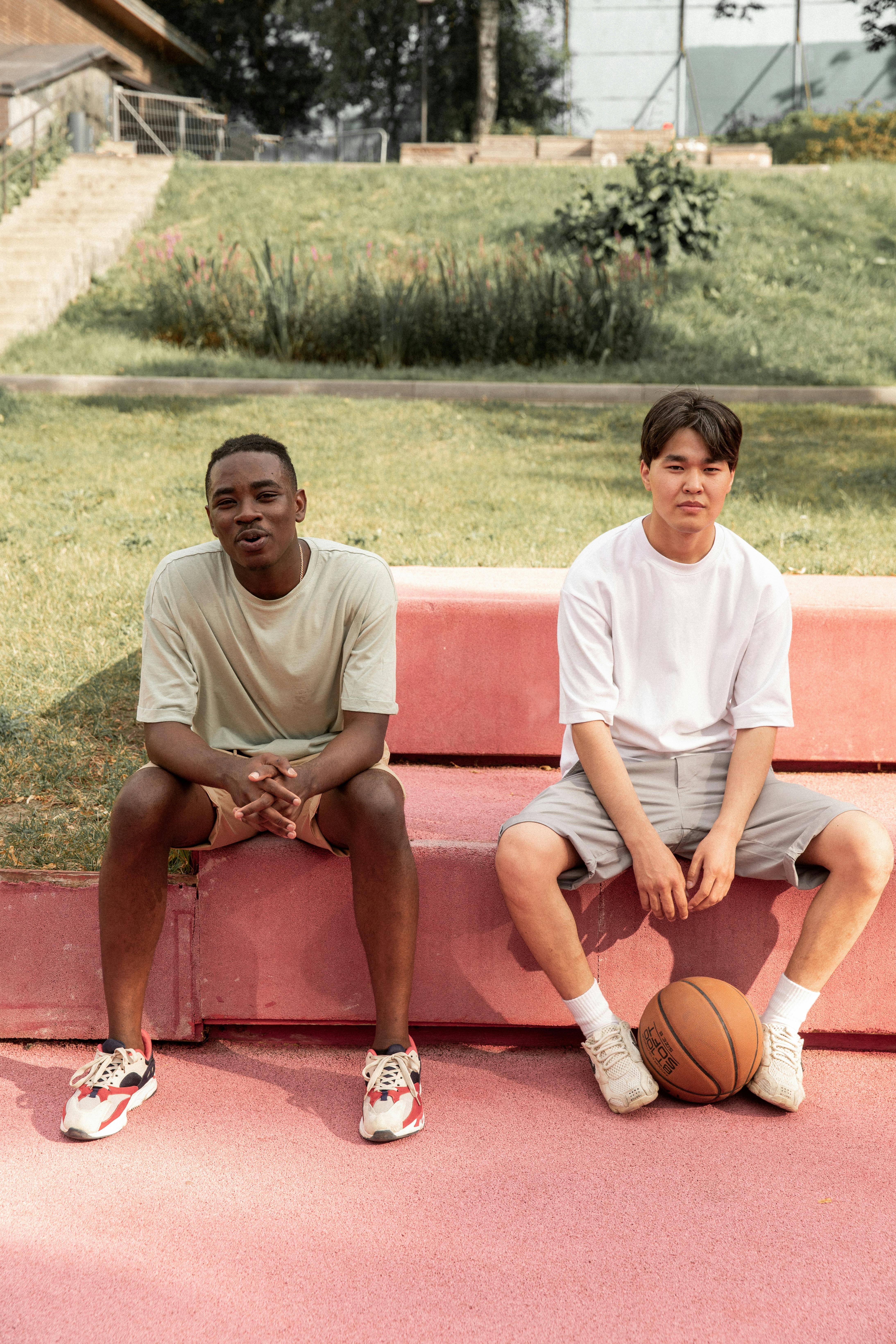 content young diverse guys relaxing on bench after basketball training