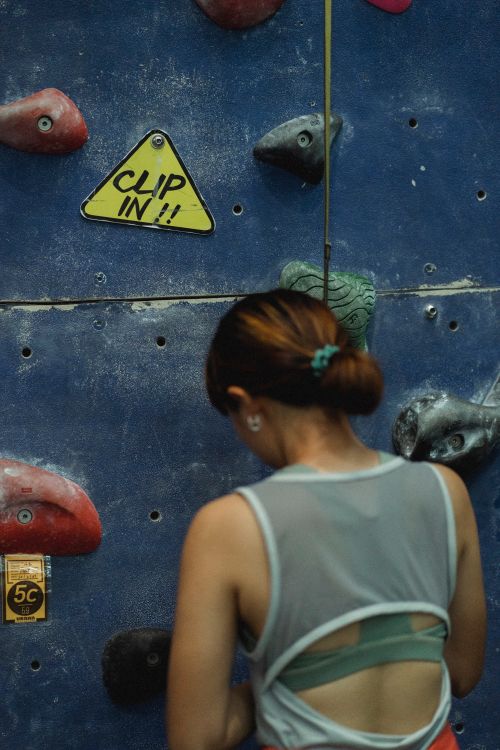 Free Back view of faceless female climber in sportswear preparing for clambering while standing near bouldering wall in gym Stock Photo