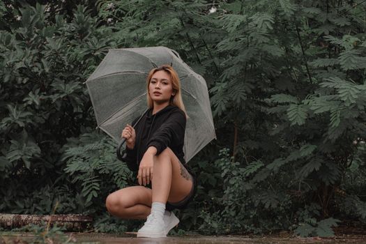 一位时尚女子撑着半透明的伞，在公园的绿荫中穿行