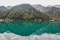 晴朗的天空下，宁静碧绿的湖中倒映着森林覆盖的山峰