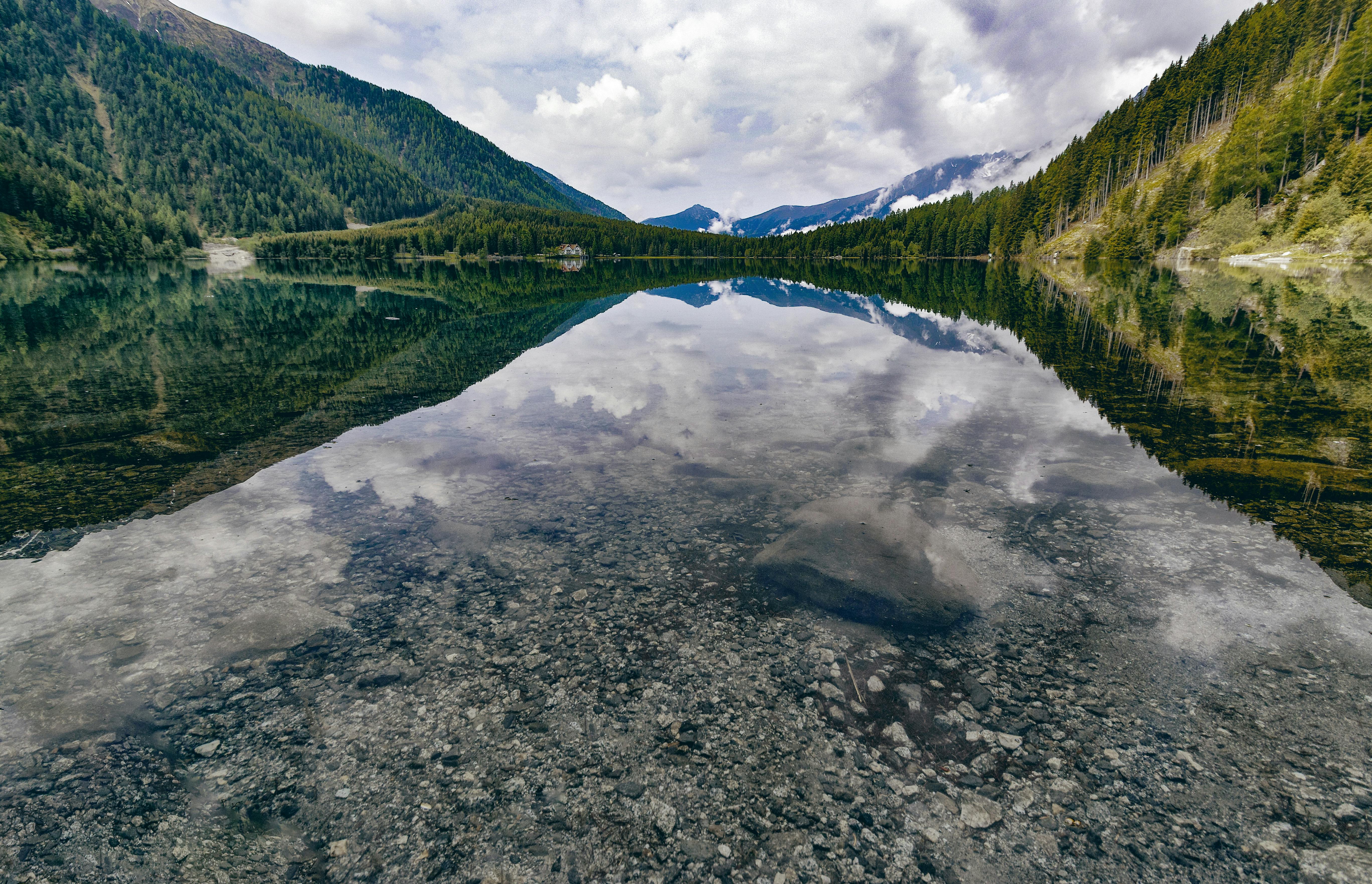 Tranquil mountain lake reflecting the cloudy sky, surrounded by lush forests.