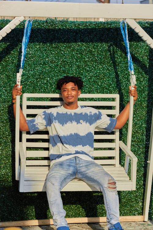 Free Smiling man in a tie-dye shirt sitting on a swing in Lagos, Nigeria garden. Stock Photo