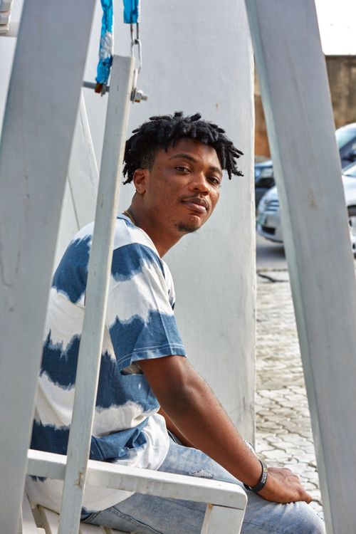 Free African man in tie-dye t-shirt sitting on a wooden swing outdoors in Lagos. Stock Photo