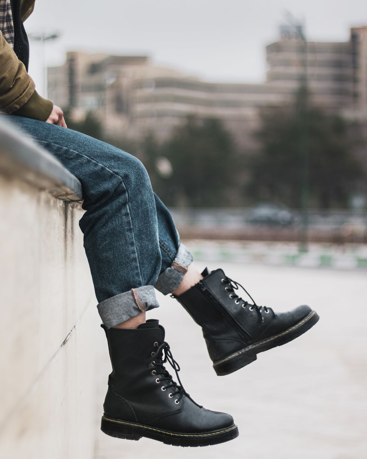 Person sitting on a concrete wall wearing cuffed blue jeans and black lace-up combat boots