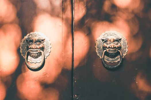 Sunlit wooden door with ornamental knockers in Beijing, showcasing cultural artistry.