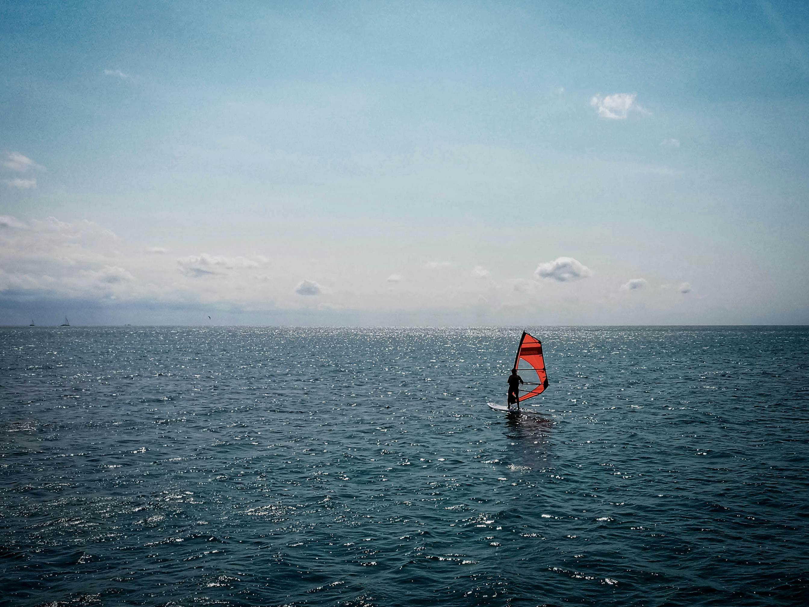 An individual windsurfing on a vast ocean under a clear blue sky, perfect for adventure enthusiasts.