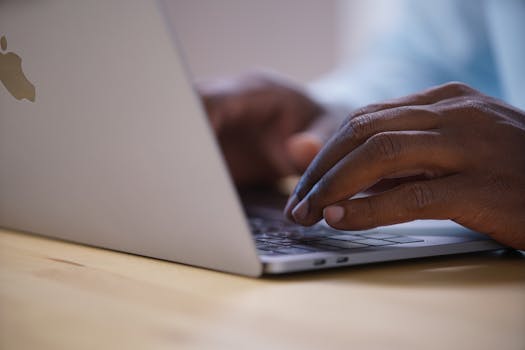 African American hands typing on a laptop keyboard on a wooden surface.