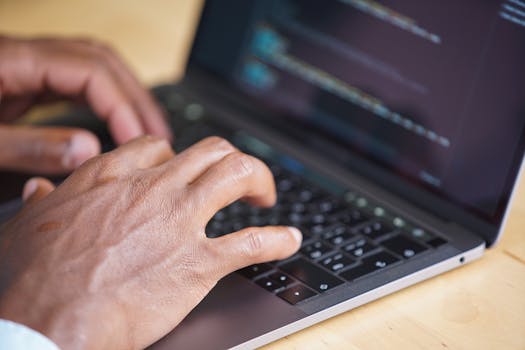 Hands typing on a laptop with code displayed on screen, showcasing technology use.