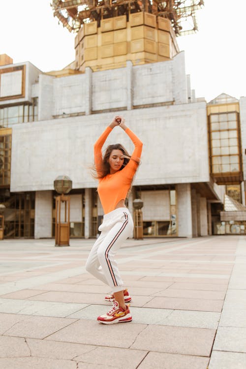 Woman in Orange Long Sleeves Dancing with Her Hands Raised