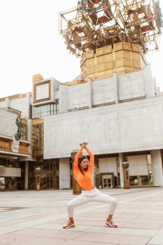一位身着活力服装的女子在城市建筑背景下摆出舞蹈姿势