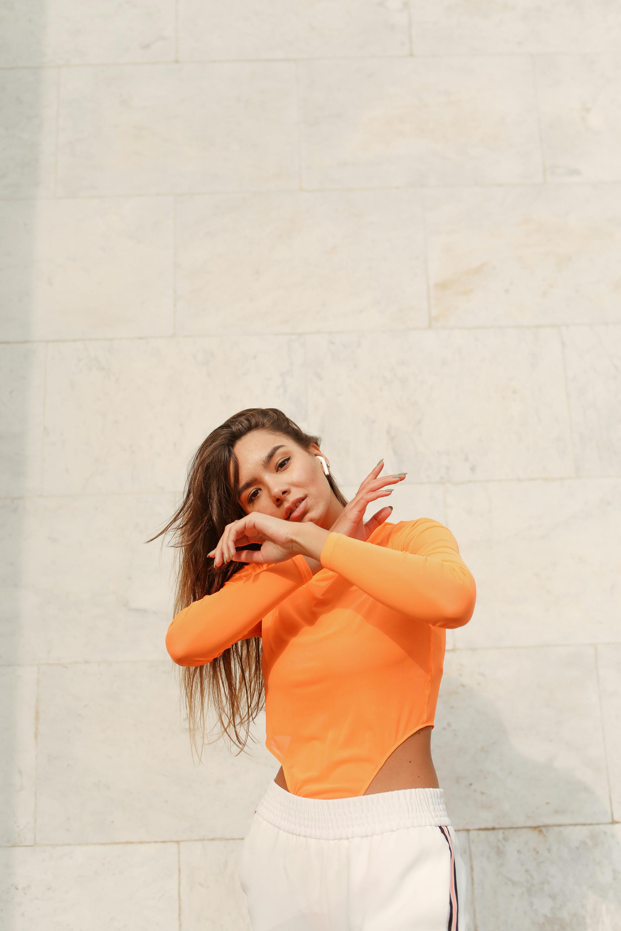 一位穿着充满活力橙色上衣的时尚女士靠在石墙上，展现了现代街头服饰风格