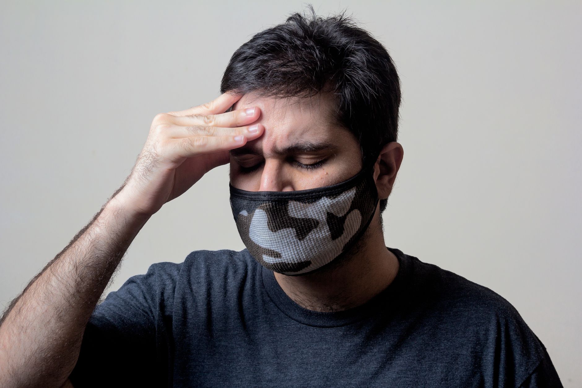 목디스크 통증, 현명하게 대처하고 건강한 일상 되찾기 6 A man in a black shirt wears a camo face mask, showing signs of headache and illness.