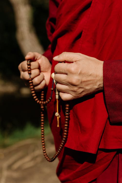 Person in Red Robe Holding a Brown Prayer Beads 