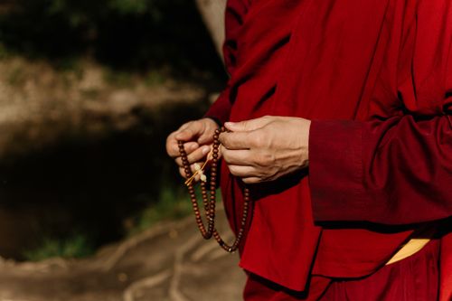Free A monk dressed in traditional robes holding prayer beads outdoors, symbolizing spirituality. Stock Photo
