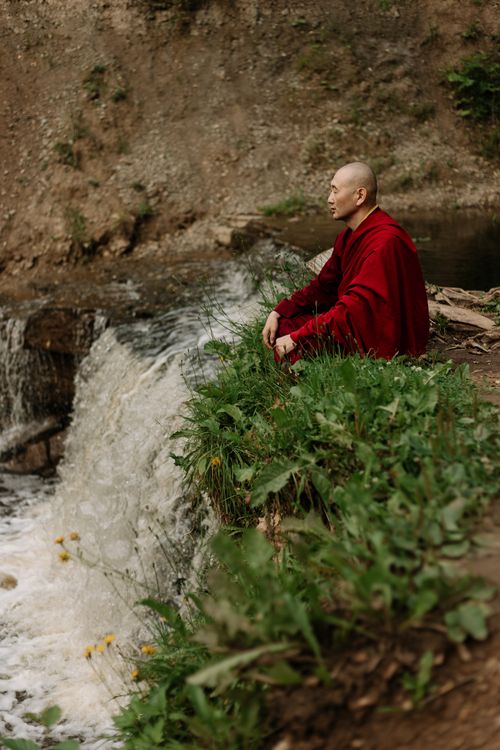 Free A Buddhist monk sits in quiet meditation by a peaceful waterfall in nature. Stock Photo