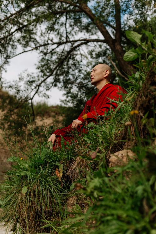 Free A monk in red robes sits peacefully amidst lush greenery, embracing solitude. Stock Photo